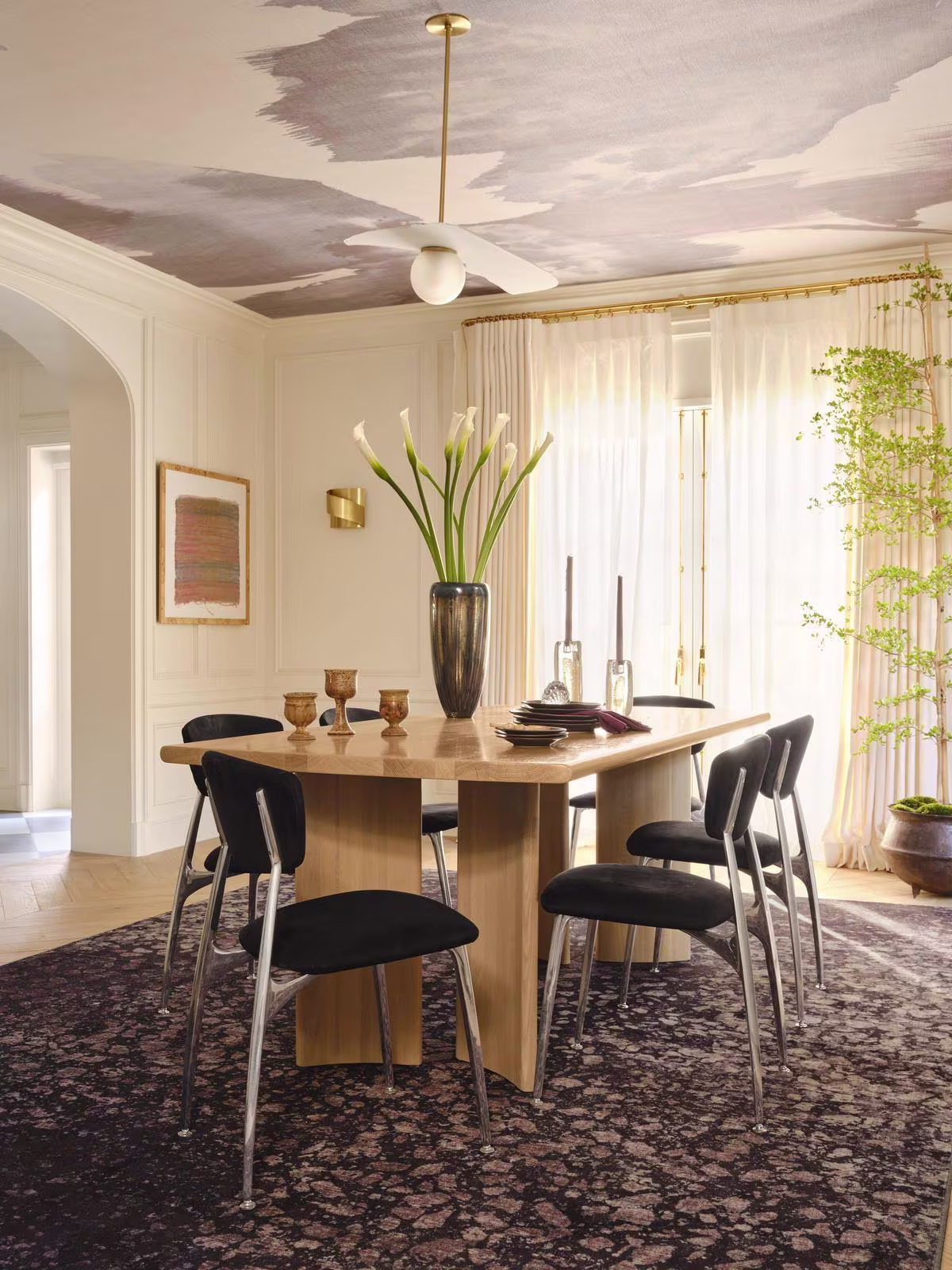 Image of a light-filled dining room with a curved entry way, wooden table, textured ceiling, and the Ruggable x Architectural Digest Terran Burgundy Rug. 