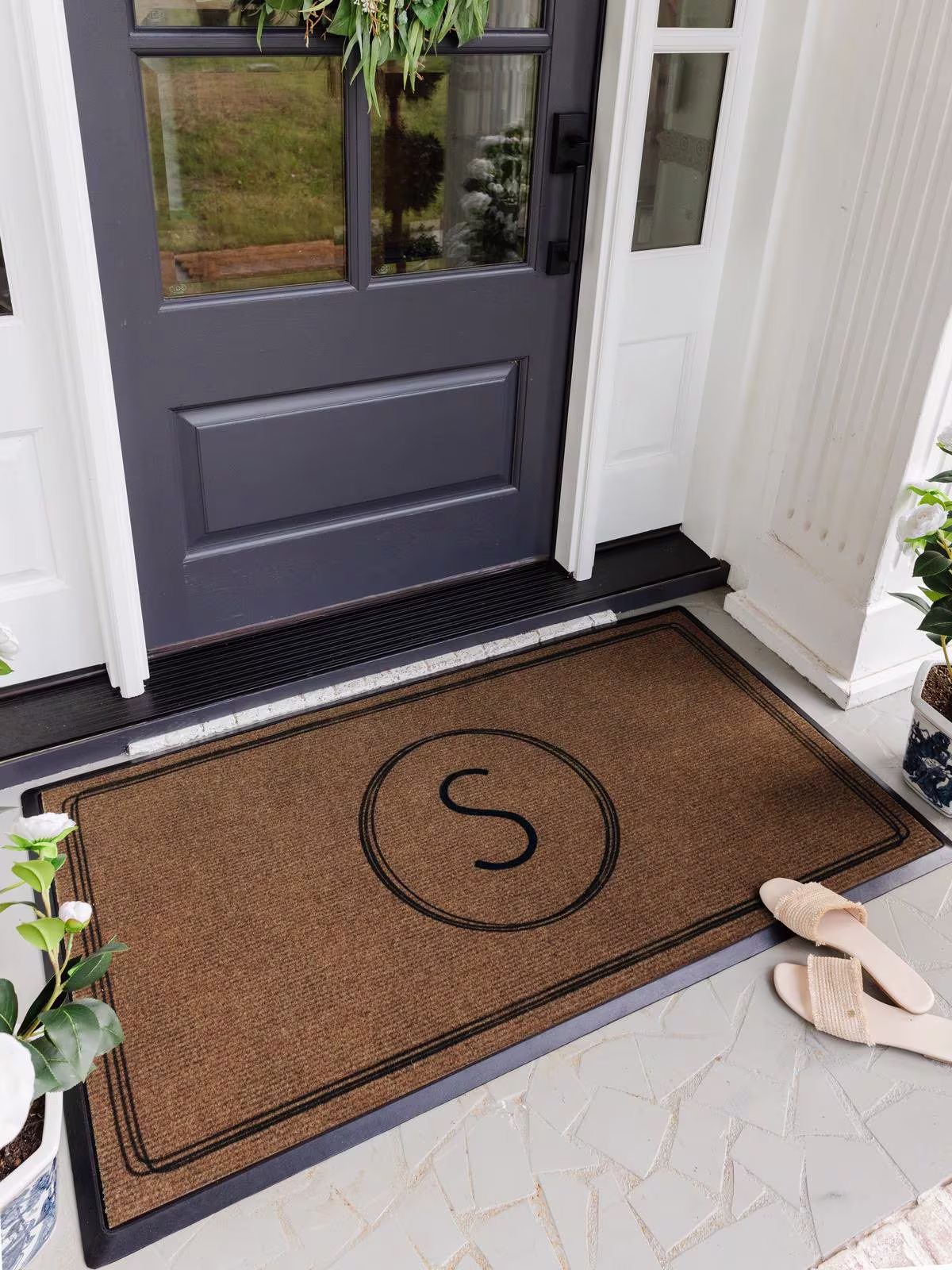 Image of a minimalist doorscape with slippers and a white fluffy dog with Ruggable's Infinity Monogram Estate Doormat.