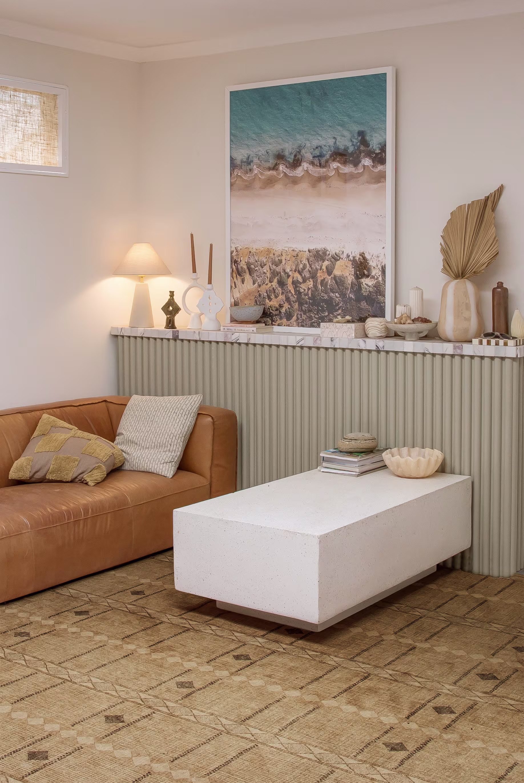 Coastal-inspired sitting area with a leather couch and neutral rug on light flooring, styled with airy, beachy decor.