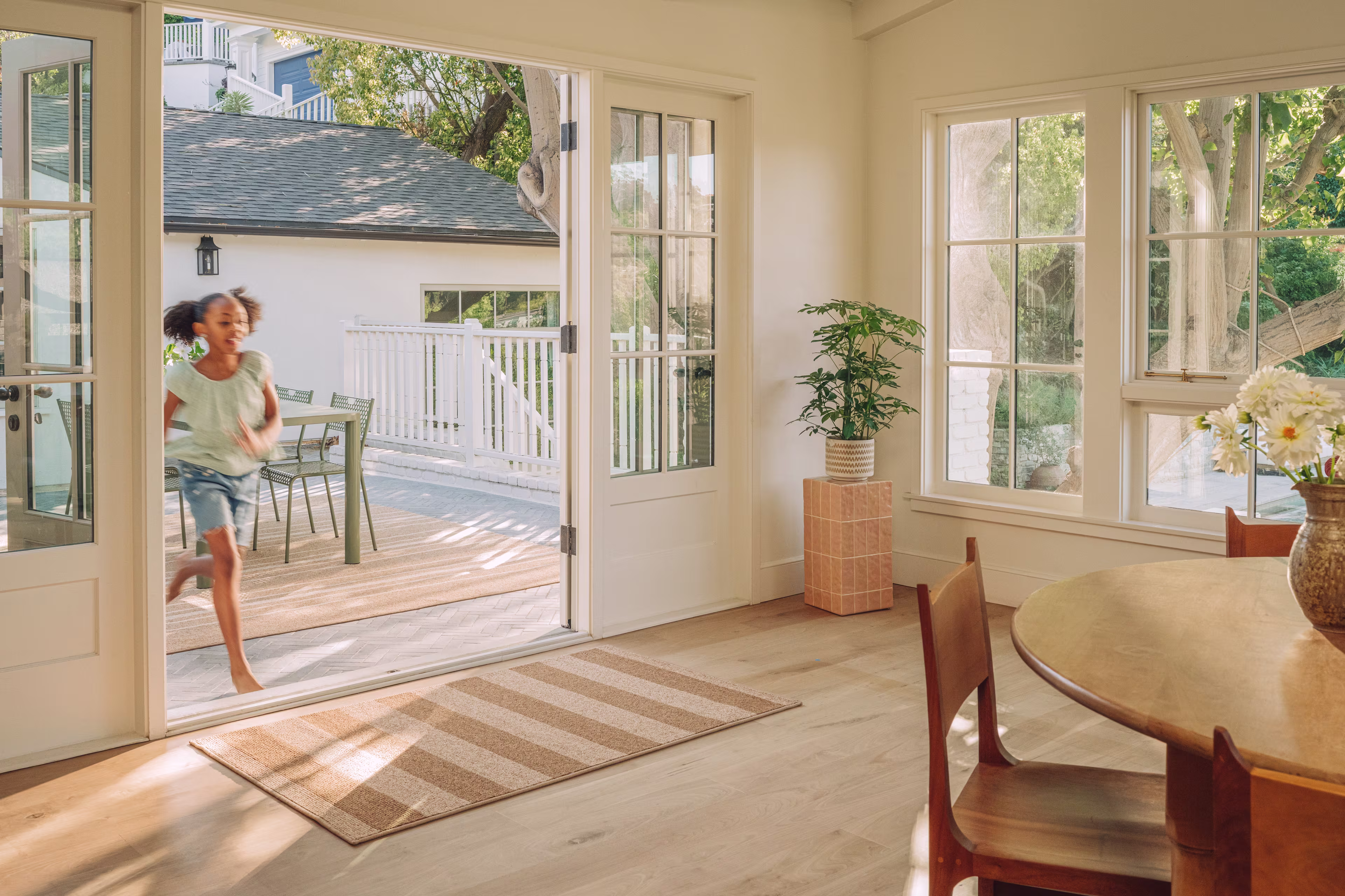 Girl entering coastal dining room from patio with tan rug at doorway.