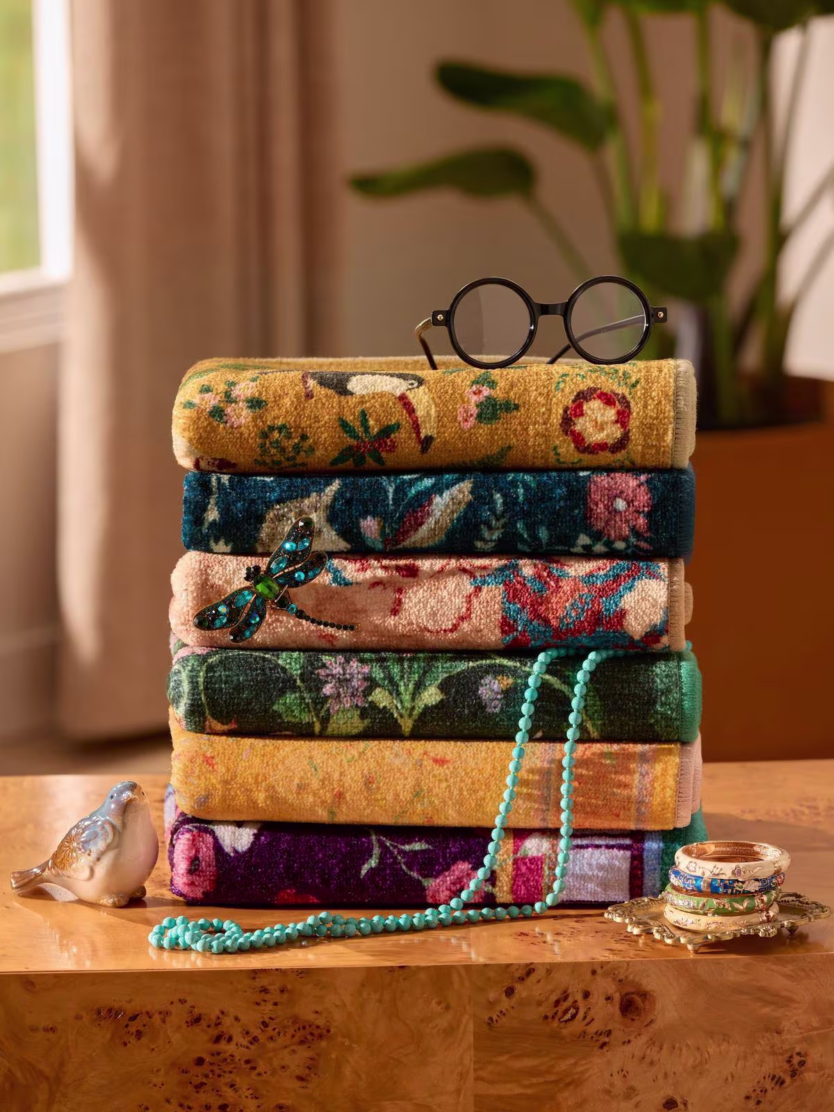 Image of a stack of Ruggable x Iris Apfel rugs with black-rimmed glasses on top and jewelry scattered around. 