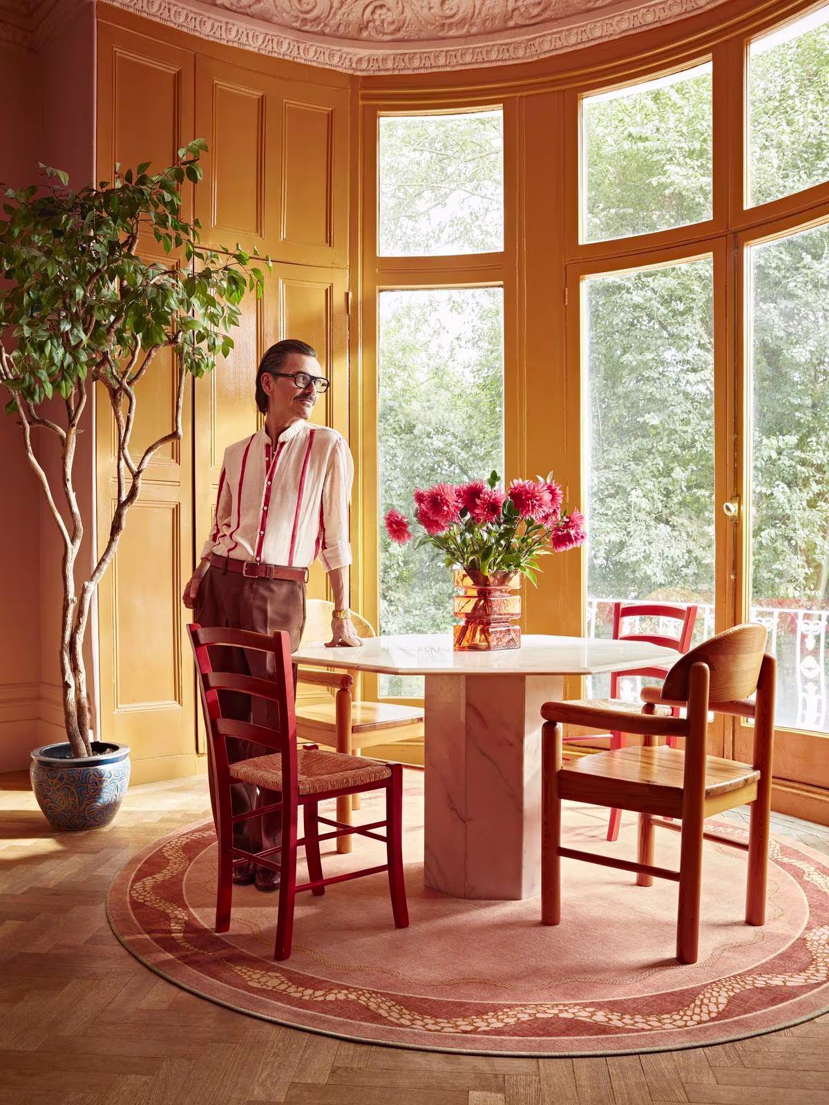 Image of a sunny dining area with wooden table and a round Matthew Williamson Serpent Border Rug beneath.