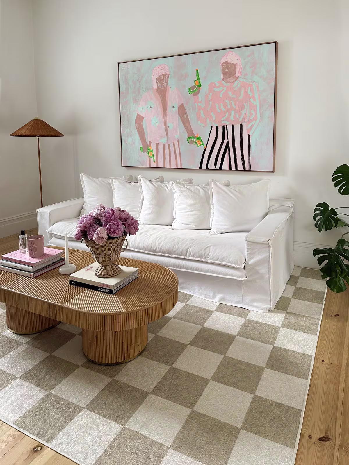 Coastal living room featuring the washable Jaque Checkered Stone Rug from Ruggable, a white shabby chic couch, rattan furniture, and pastel wall art. 