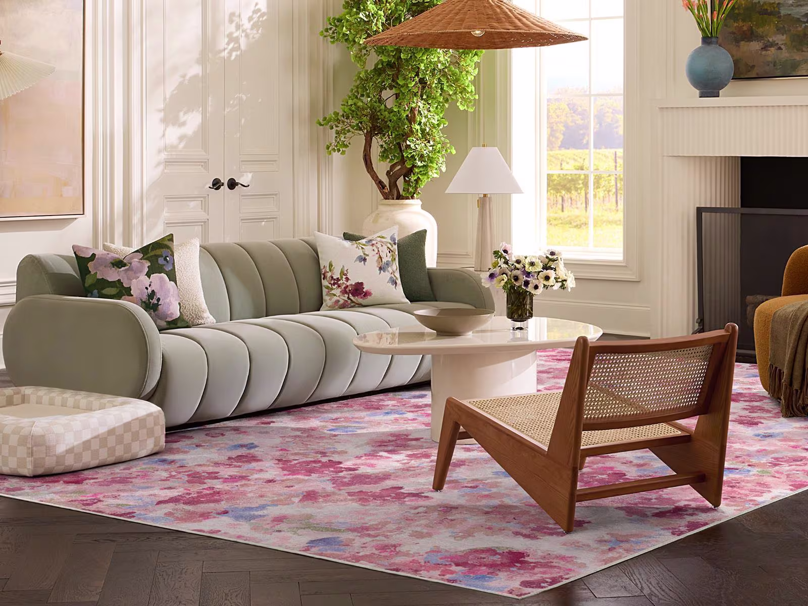 Image of a sunlit living room with a plush light green sofa, checkered dog bed, and the floral Camille Multicolor Pink Rug. 