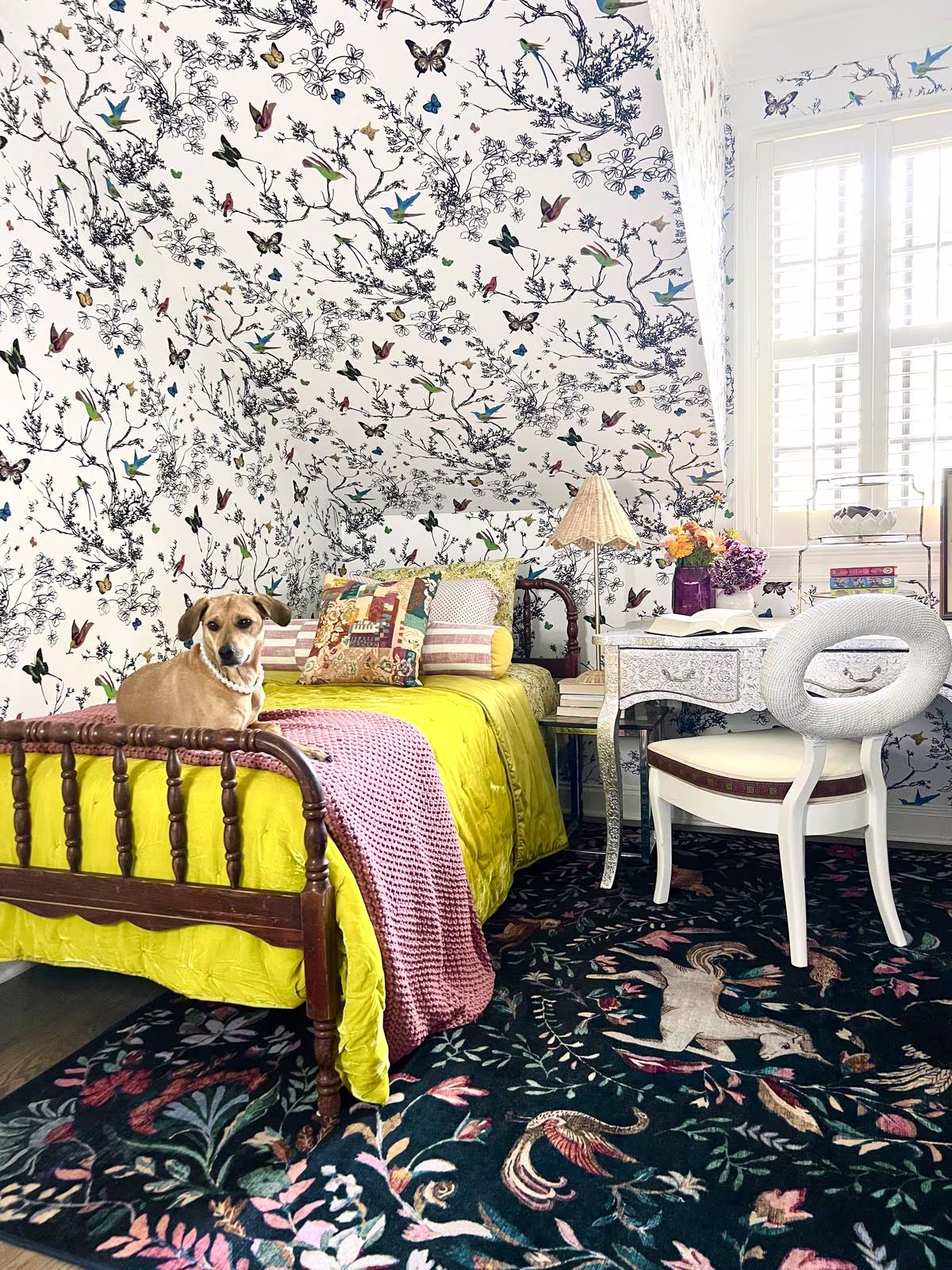 Bright maximalist children's bedroom with a twin bed, dog wearing a pearl necklace , floral wallpaper, and the Ruggable x Iris Apfel Dreamweaver Blue Multicolor Rug.