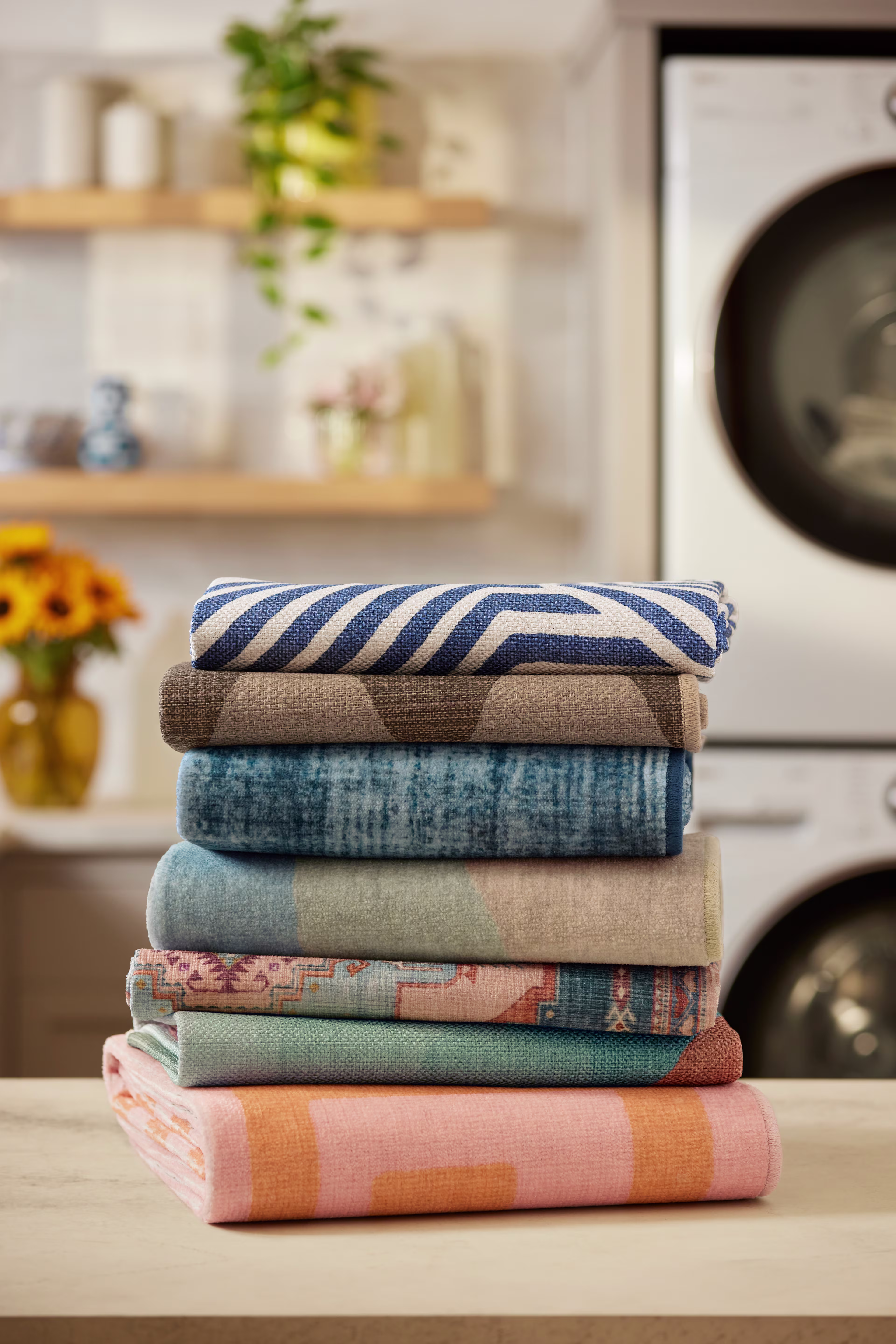 Stack of colorful washable rugs arranged in a laundry room, showcasing multiple styles ready for machine washing