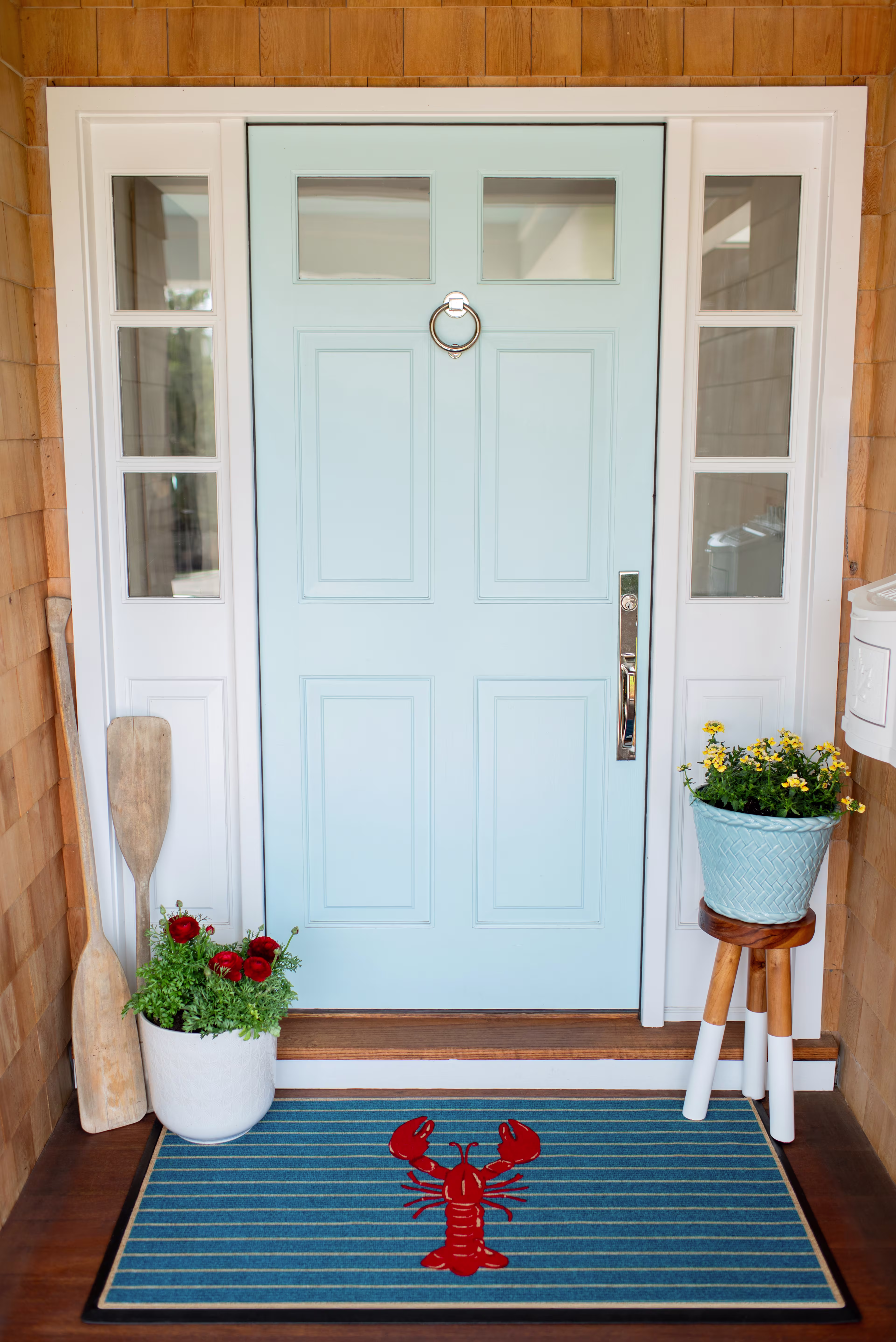 Blue doormat with a red lobster placed in front of a coastal-style entryway.