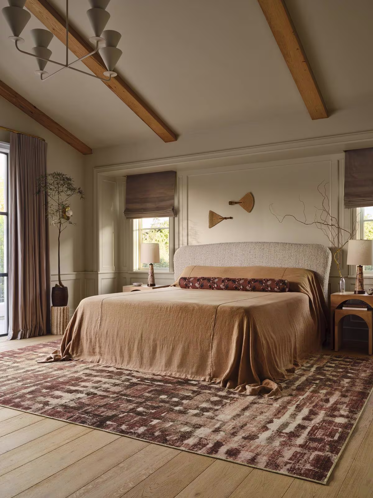 Image of a bedroom with the Ruggable x Architectural Digest Brooklyn Copper Clay Rug on top of a light wooden floor, with a lofted ceiling, minimal decor, and a bed with a light orange bedspread. 