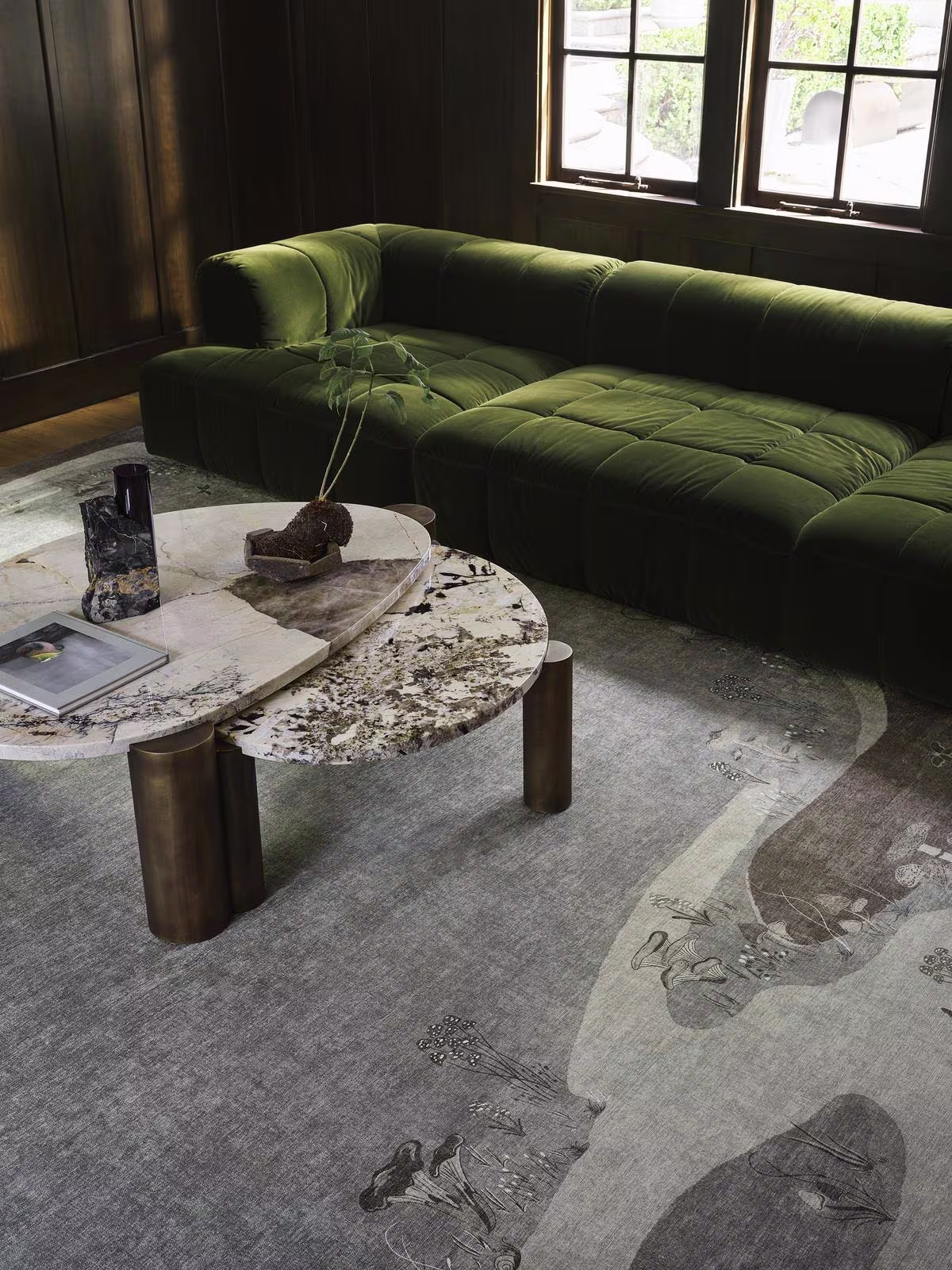 Image of a moody living space with a dark green velvet couch, a large marble coffee table, and the Ruggable x Architectural Digest Mushroom Dream Grey Taupe Rug.