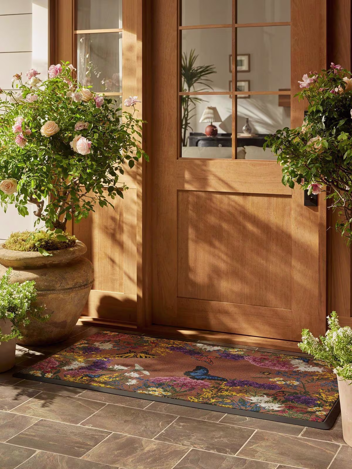 Image of a sunny doorstep with blooming roses and Ruggable's Meadow Multicolor Estate Doormat.