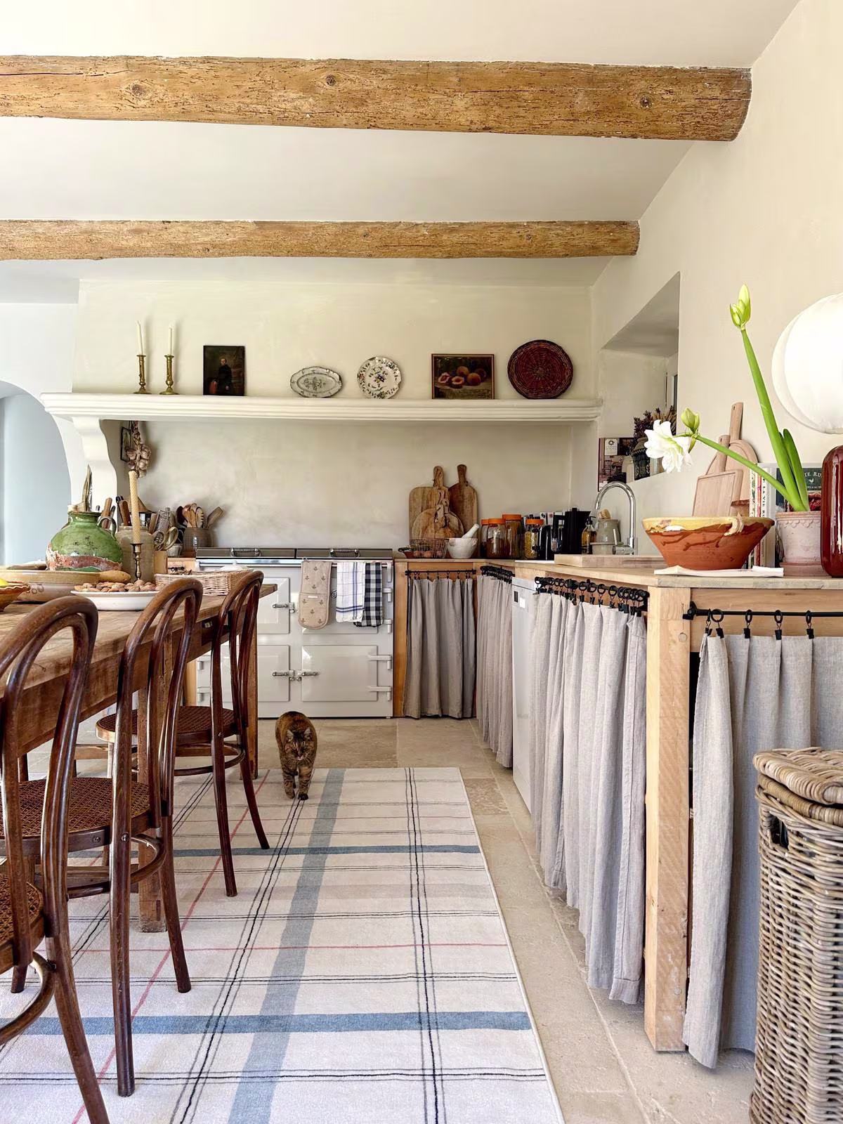 A rustic French kitchen with washable Ruggable Irene Plaid Ivory & Blue Multicolor rug, wooden furniture, and cat