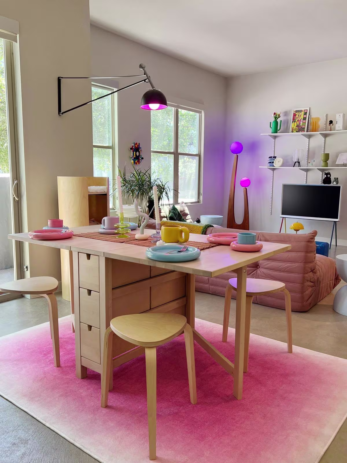 Image of living room and dining table with futuristic elements, pops of bright colors, and the Ruggable x Barbie™ Pink Ombre Tufted Rug.