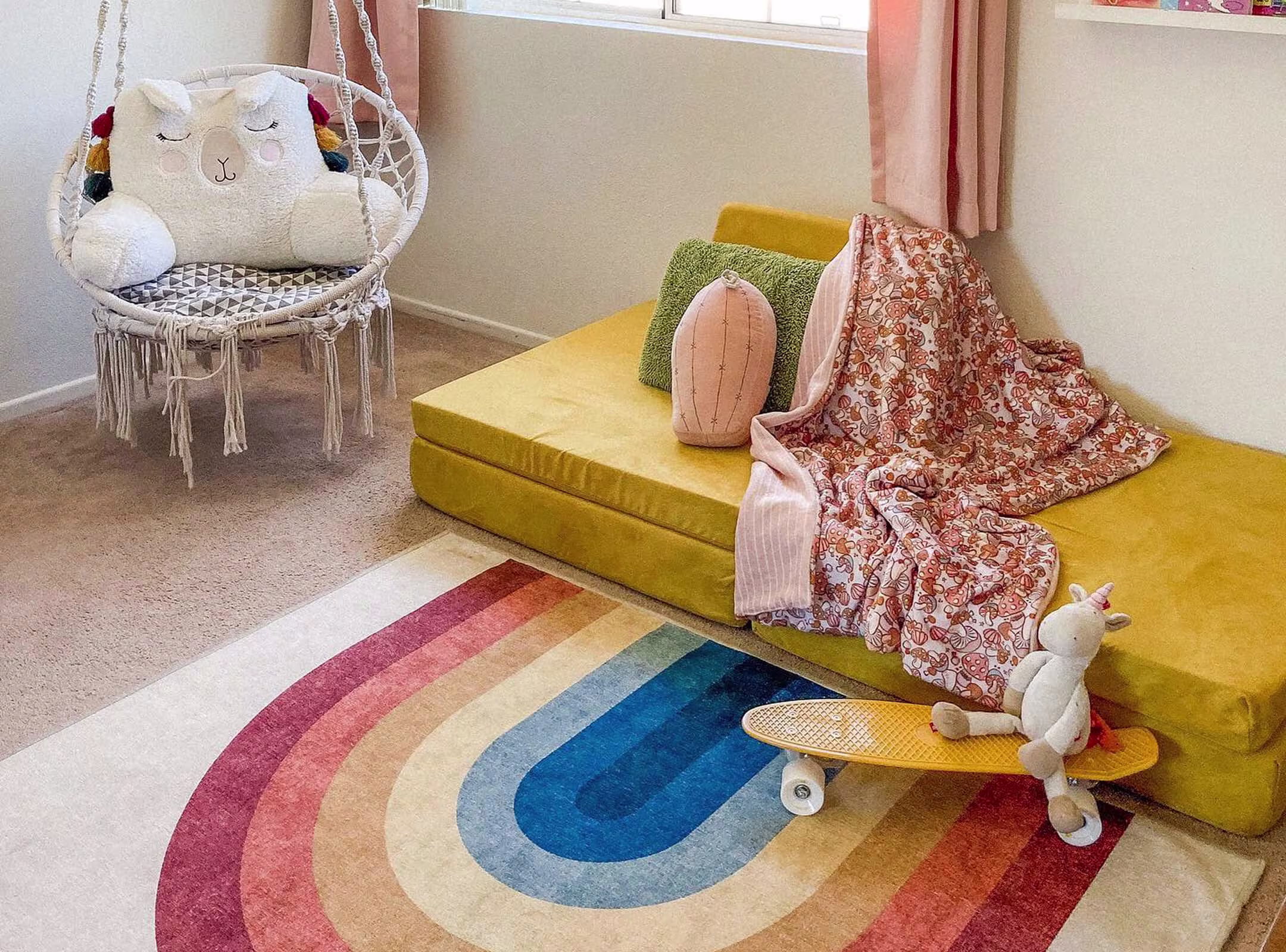 Absida Rainbow Multicolor Rug with bold arching stripes in red, orange, yellow, and blue, placed on a beige carpet in a cozy kids’ playroom.
