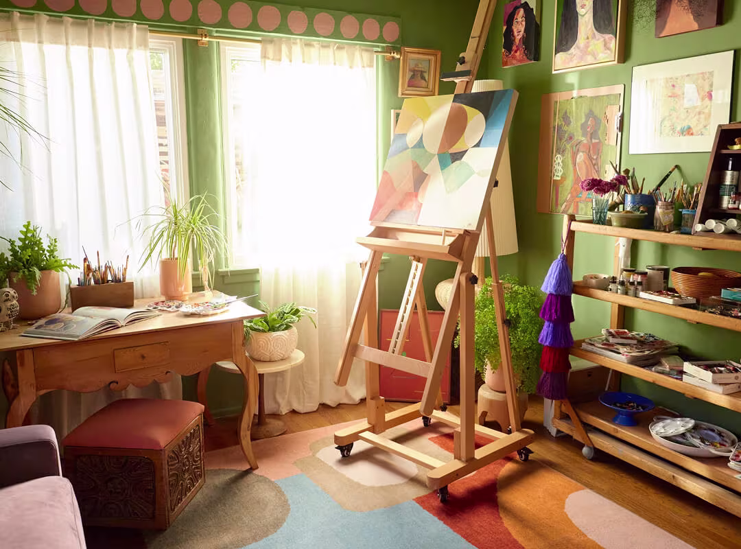 Colour drenched creative studio with sage green walls, art-filled shelves, and a Sonia Terra & Sage Rug by Justina Blakeney bringing boho pattern and warmth to the space.