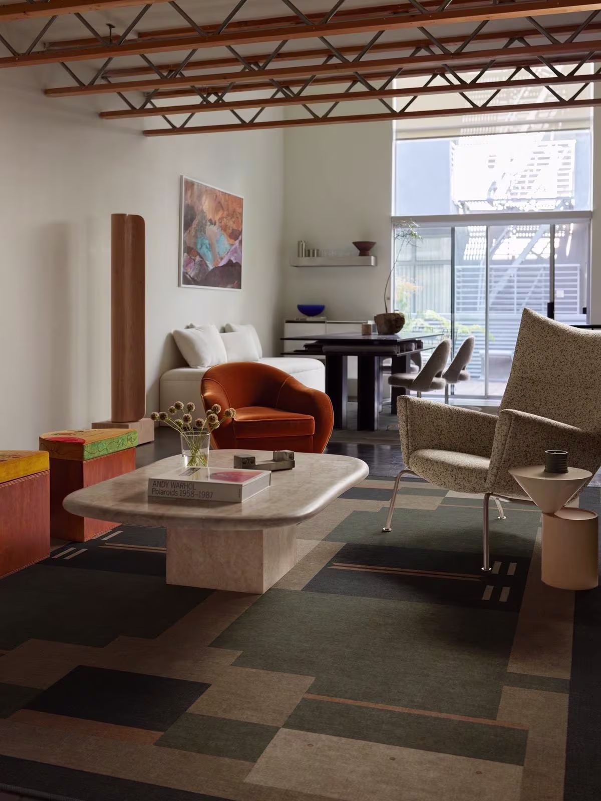 Image of a loft-style living room and work space featuring exposed ceilings, white walls, curved neutral furniture with metal accents, and the Ruggable x Architectural Digest Monolith Olive Green Rug. 
