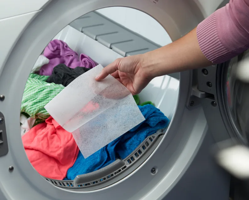 Dryer sheet being added into a dryer full of clothes