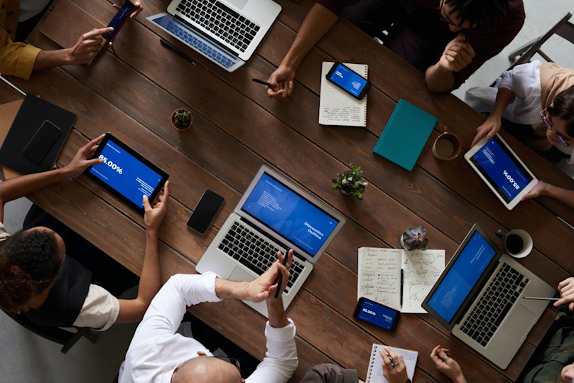 a group of people sitting around a table with laptops