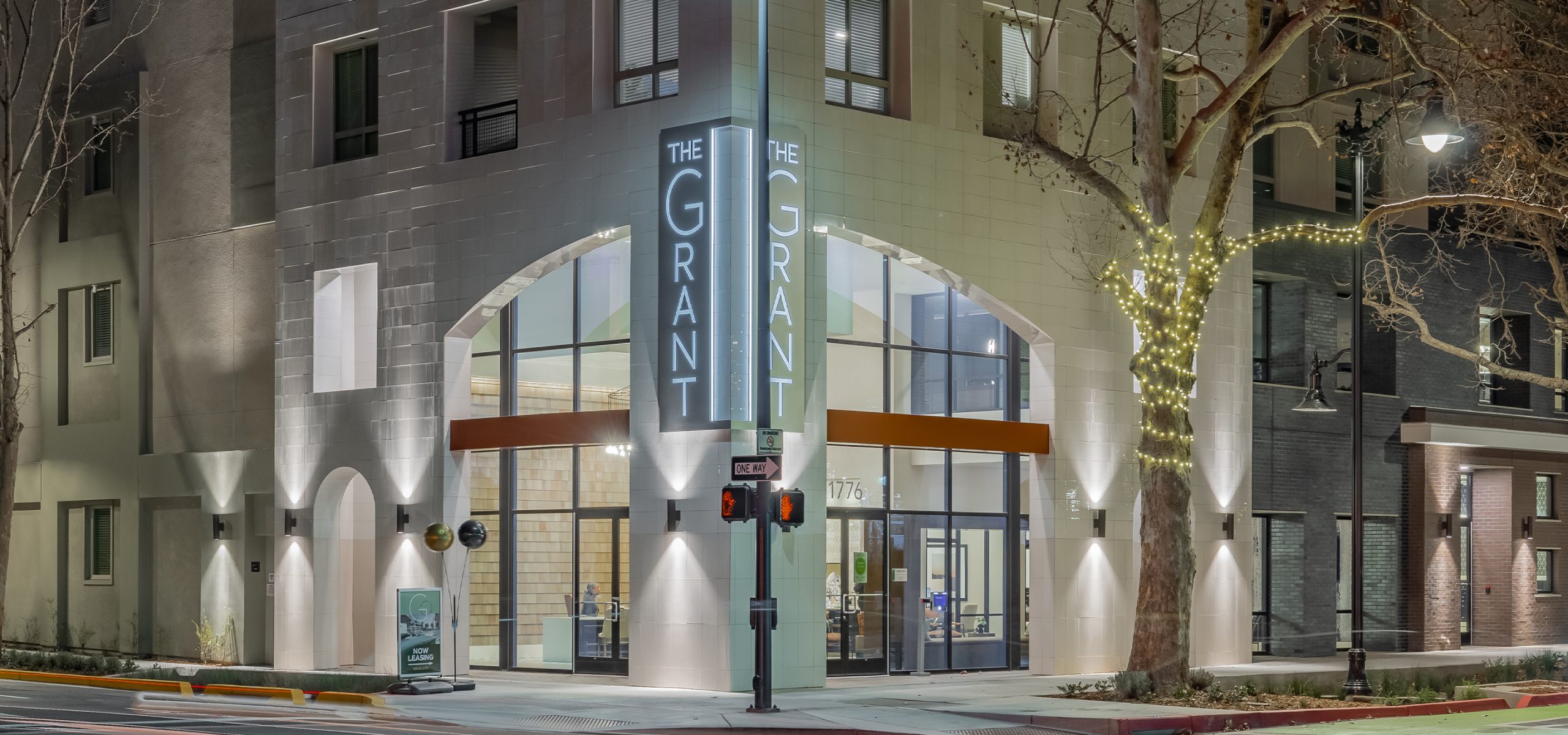 Night view of The Grant’s illuminated entry with modern signage and arched glass facade—highlighting the project’s upscale design and leasing center.