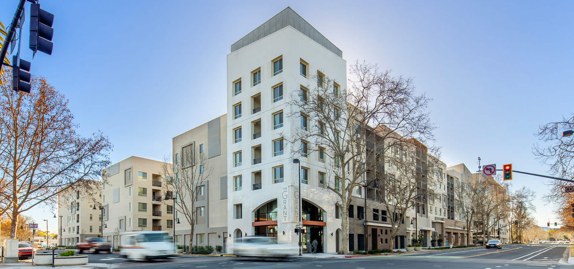 Modern multifamily apartment building in downtown Concord with clean white facade, arched entry, and tree-lined street at a busy intersection.