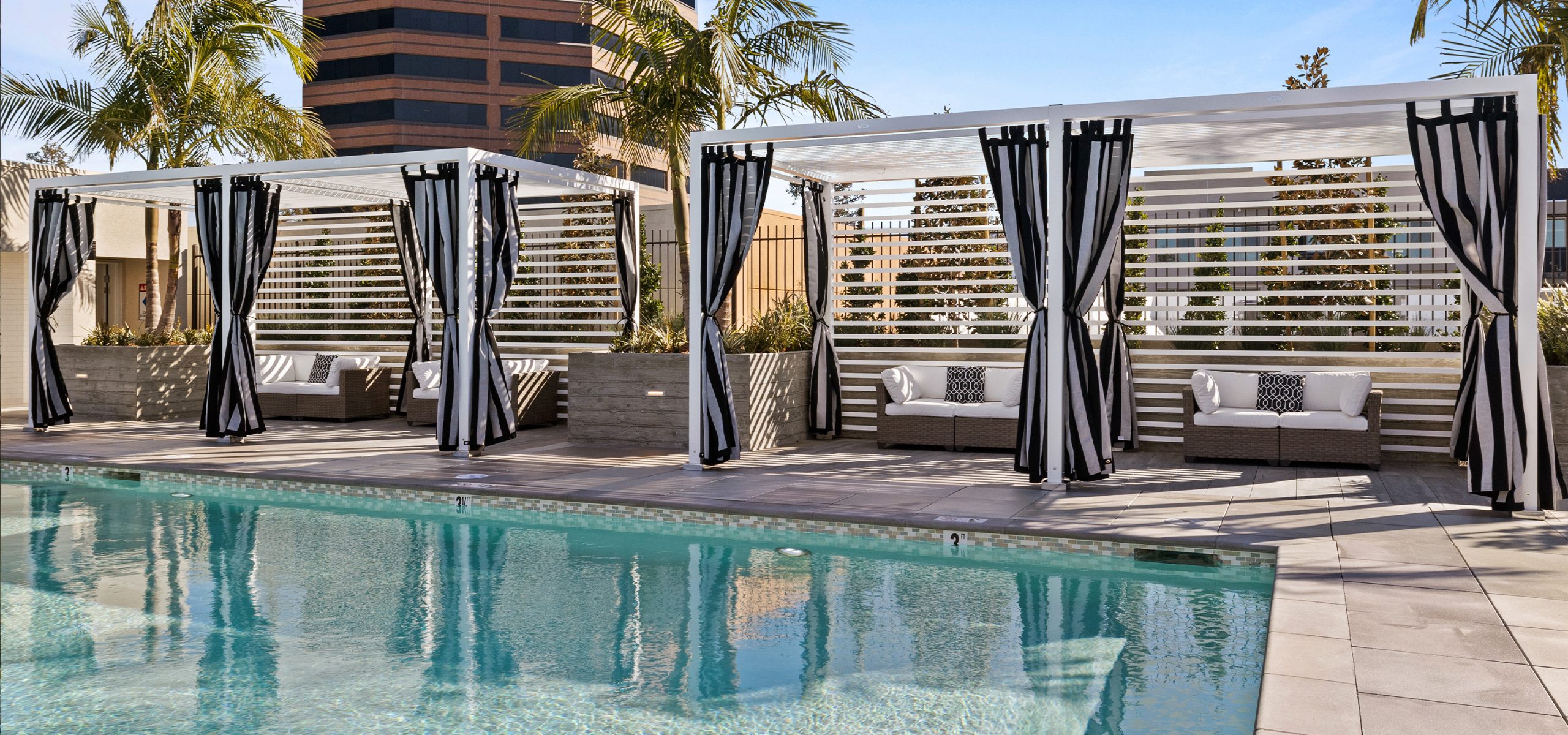 Resort-style rooftop pool deck with striped cabanas and palm trees at The Grant—showcasing the premium amenities enabled by smart infill development strategy.