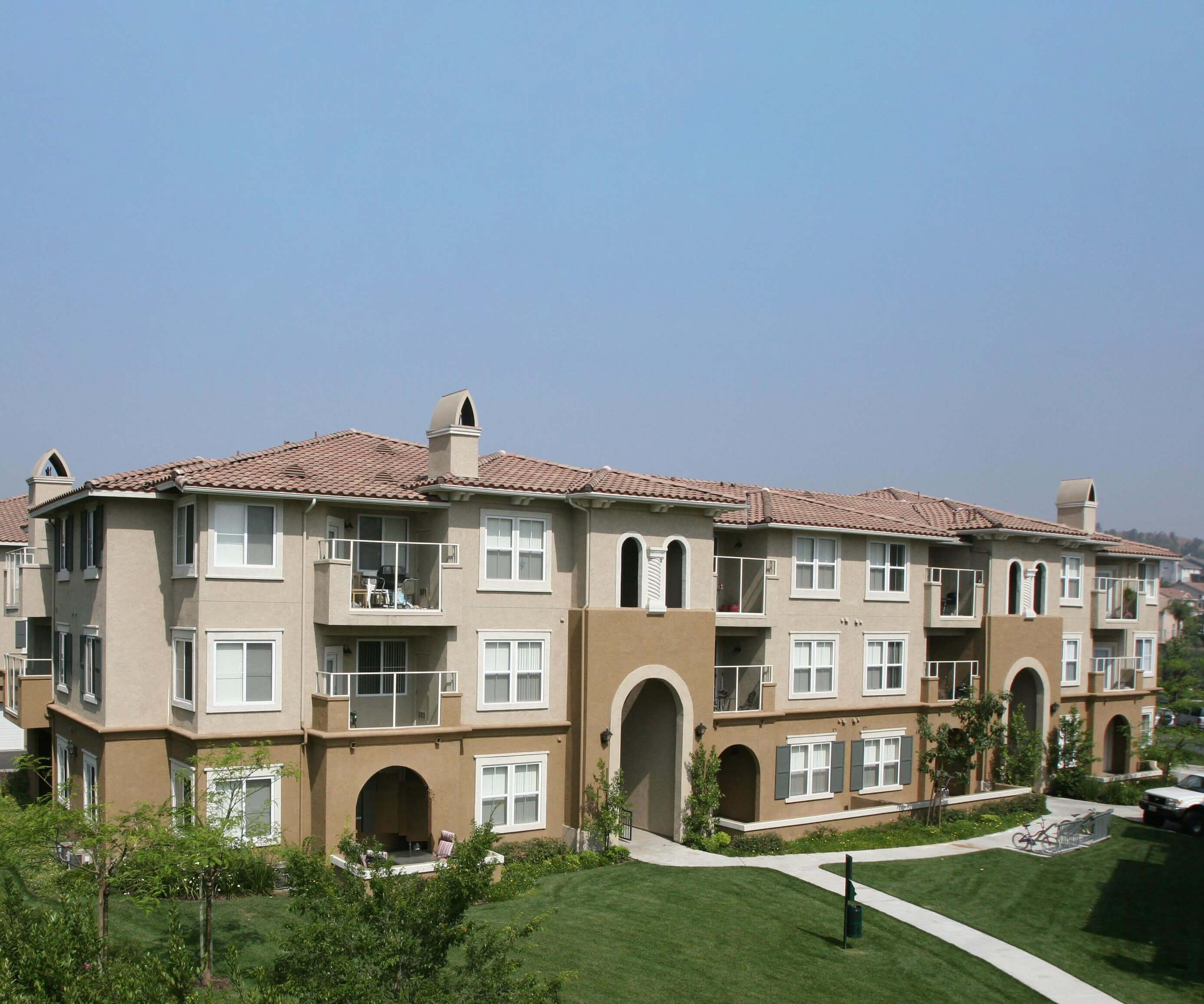 Suburban multifamily development with Spanish-style architecture and tile roofs, featuring green space and walkable paths in the Inland Empire.