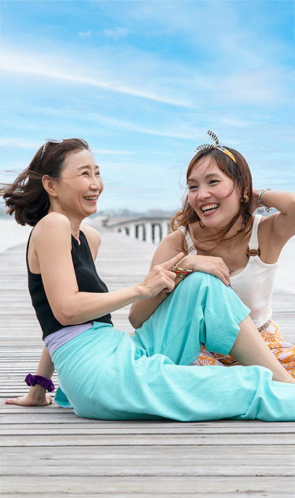 Maman et sa fille souriant, assises sur la plage