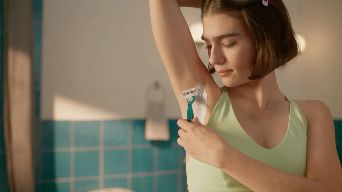 Smooth razor video thumbnail showing a woman with short hair in a green top, shaving her armpit