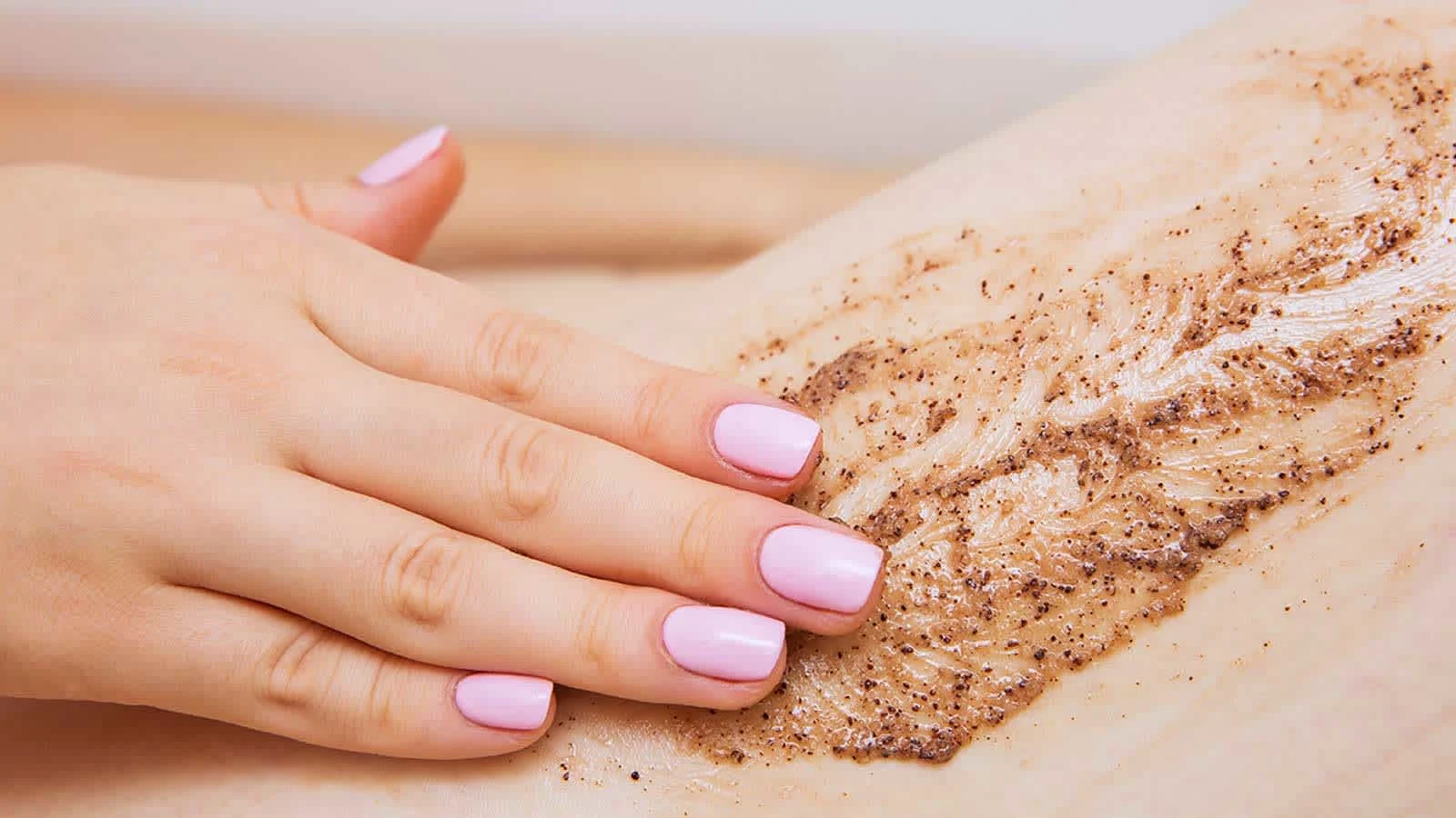 Female hand applying a brown scrubbing product onto her leg