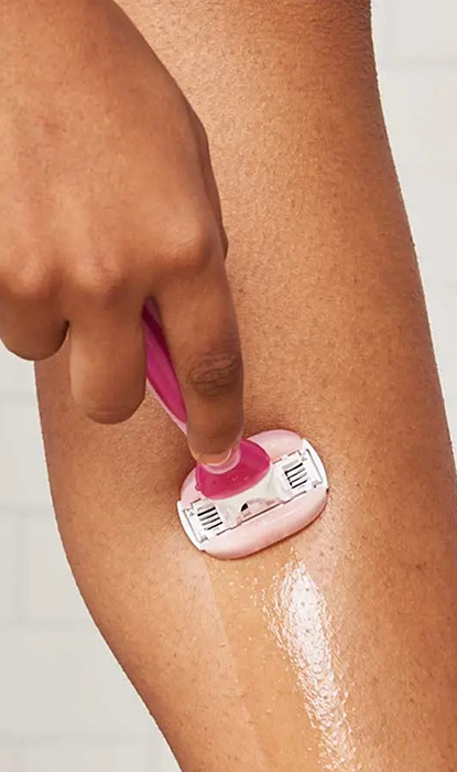 Gros plan d'une main utilisant un rasoir rose Gillette Venus pour raser le mollet