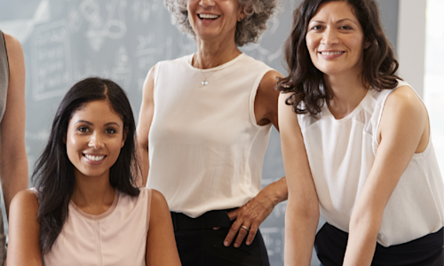 Three women sit and stand around a table at their workplace