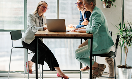Middle age couple sitting at high top table looking at laptop with financial advisor