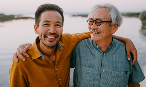 Smiling senior father and adult son on beach