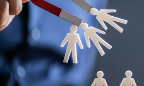 Person in a blue shirt holds a magnet that is attracting paper doll people