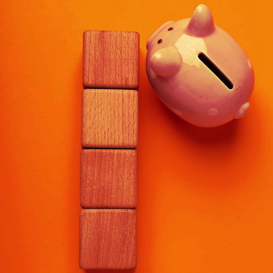 Pink piggy bank beside stacked wooden blocks on an orange background, symbolizing budgeting and the cost of ongoing website maintenance Pink piggy bank beside stacked wooden blocks on an orange background, symbolizing budgeting and the cost of ongoing website maintenance