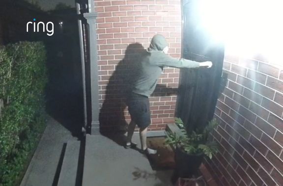 A person in a green hoodie and hand over their face approaches a home and tries to open the door. He then checks the side door and is deterred by the automatic outdoor lights, and runs away.  All recorded on the Outdoor Camera Plus featuring retinal 2K.