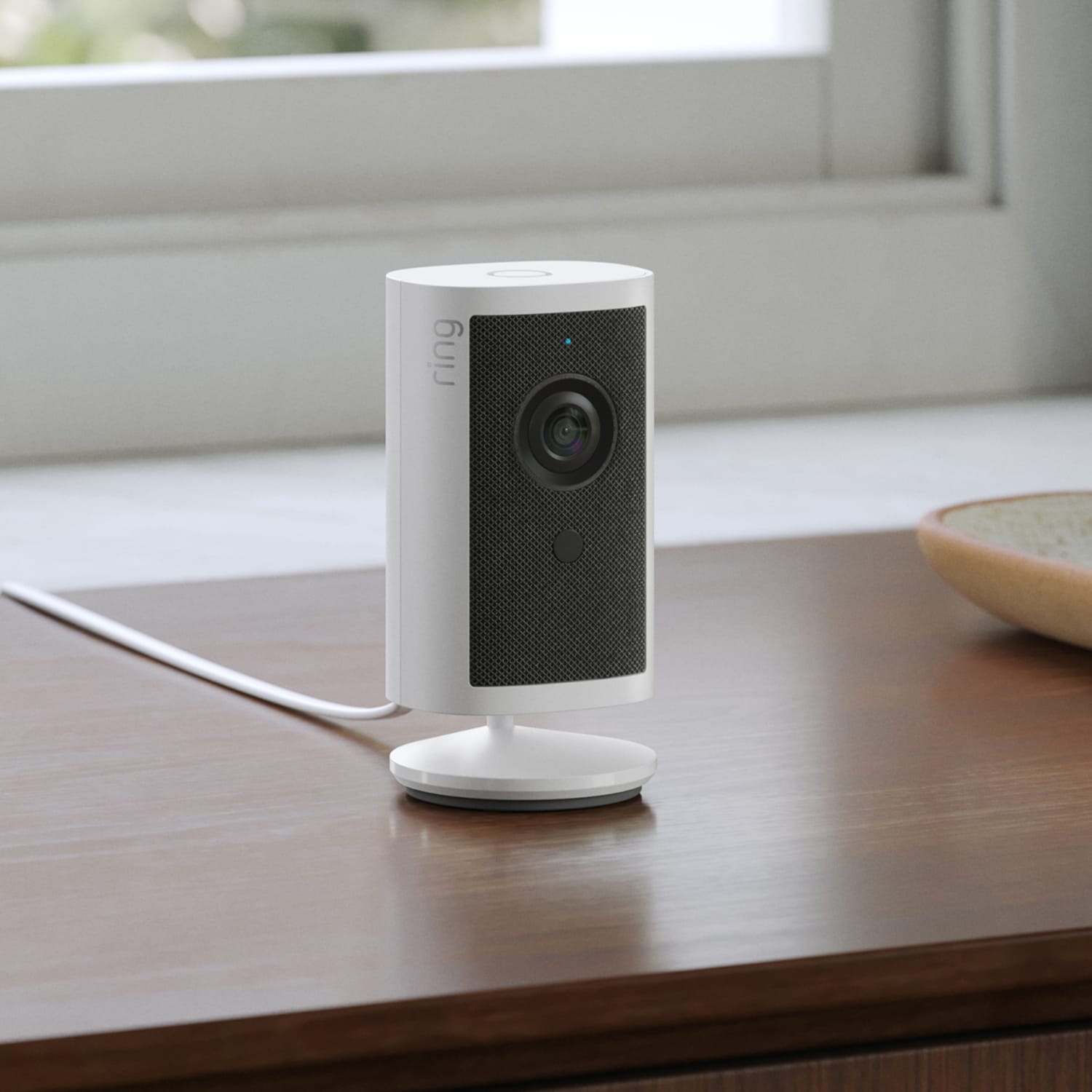 PoE+ to USB-C Indoor Adapter (Indoor Cam 4K, Outdoor Cam 4K Plus, Outdoor Cam 4K Pro, Outdoor Cam Plus) - White indoor security camera on a stand, plugged in and sitting on a wooden table near a window and ceramic dish.