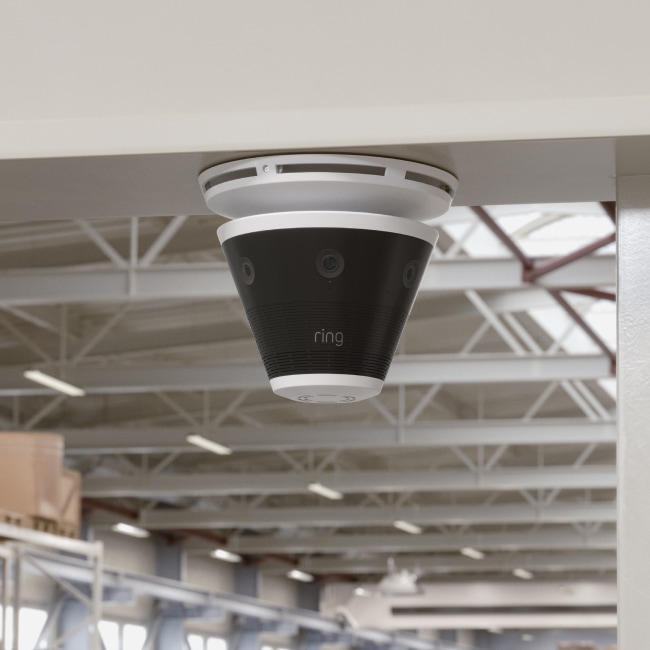 Ring security camera mounted on ceiling in commercial space with exposed metal rafters and industrial lighting.