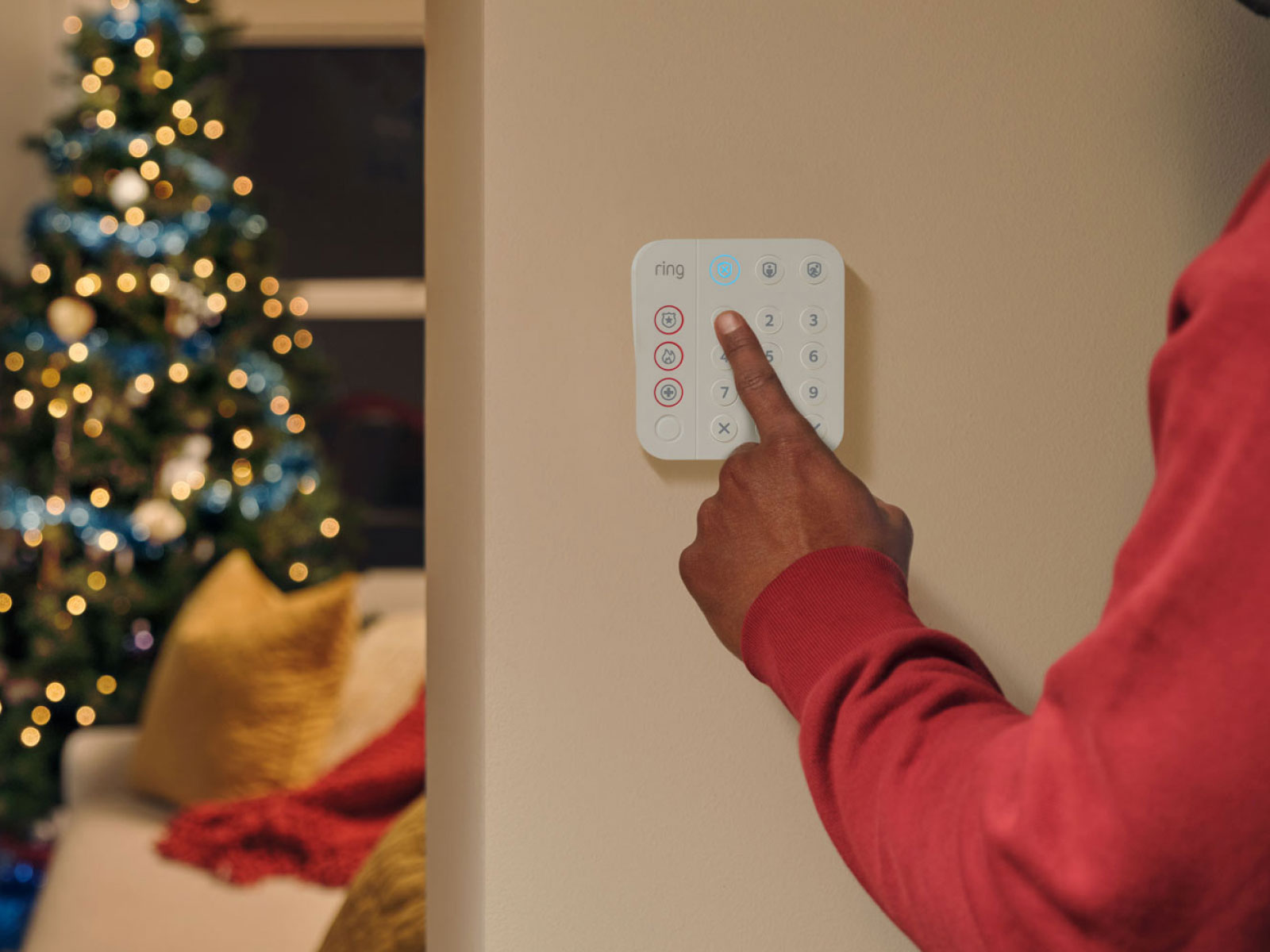 A person pressing on a white alarm keypad, with a christmas tree in the background.