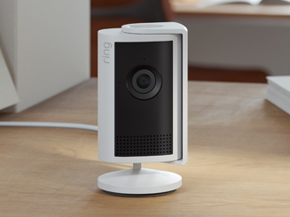 white Indoor Camera Plus with cover open placed on table with plug-in cord trailing behind