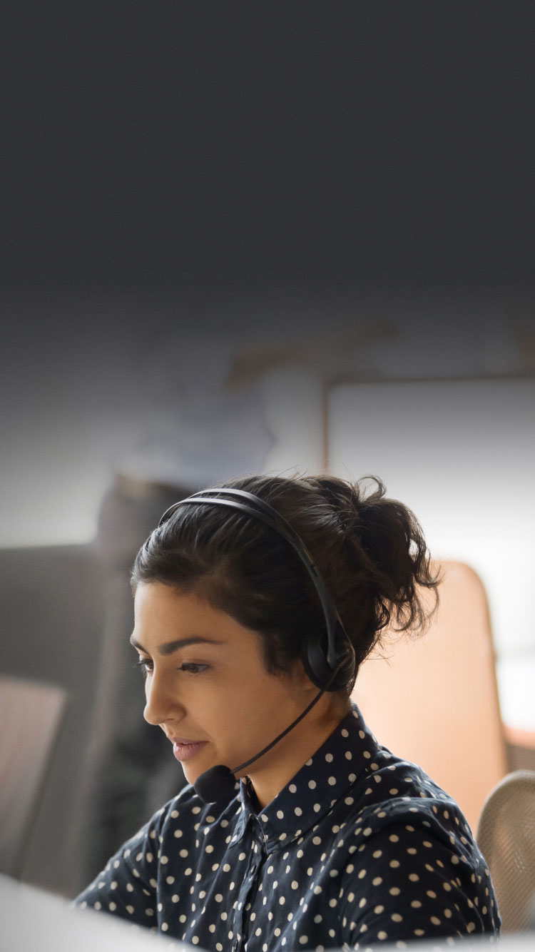 A woman wearing a phone headset sits in a call center responding to a call.