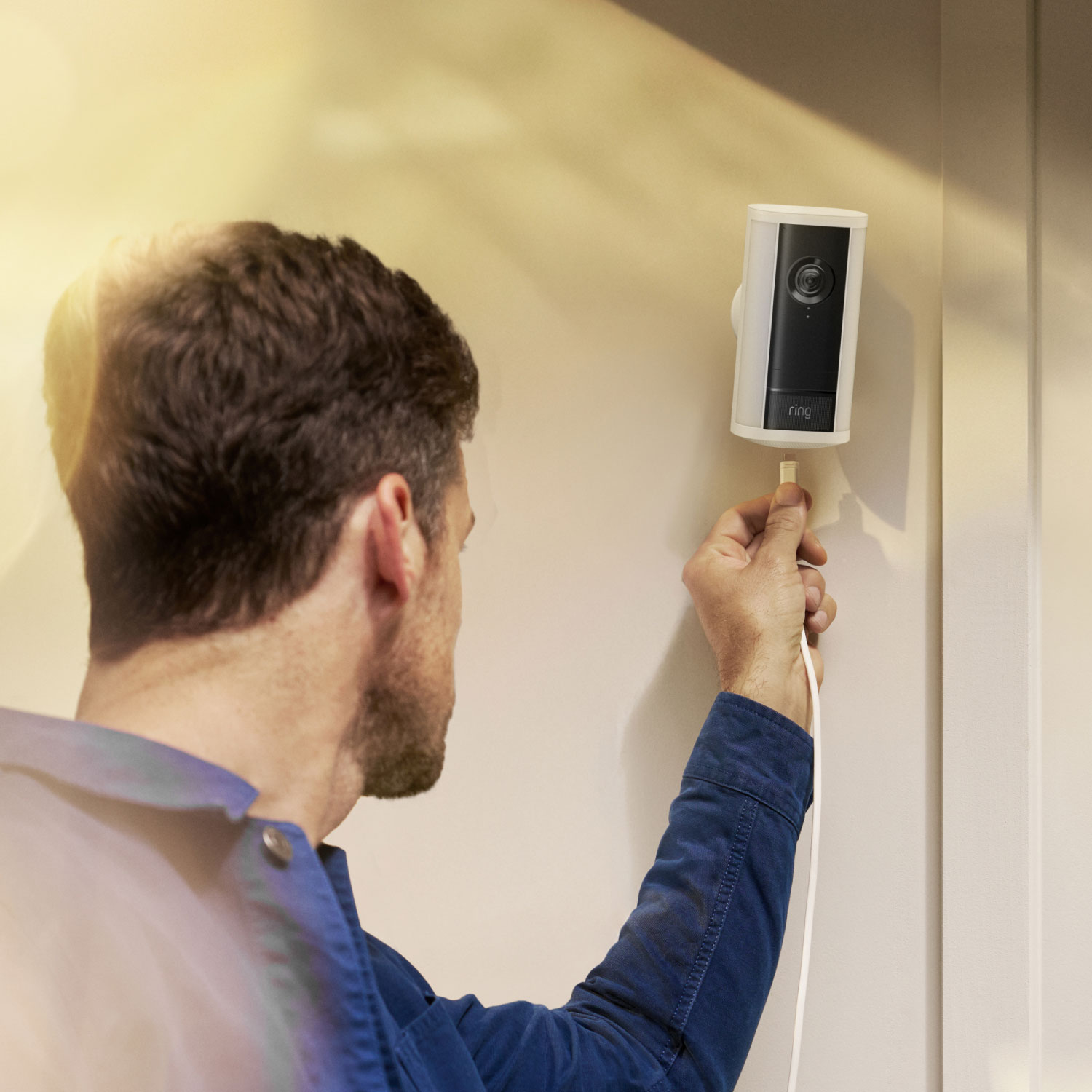 Man on a ladder mounting a white Spotlight Cam Pro (2nd Gen) onto the side of his home. 