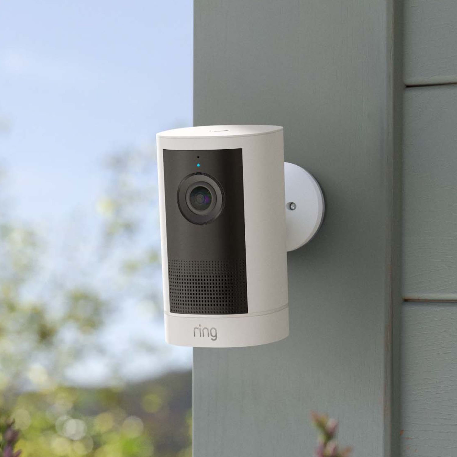 Outdoor Cam 4K Plus  - Power over Ethernet:White Ring security camera mounted on an exterior wall, lens centered with black panel, outdoor background softly blurred.