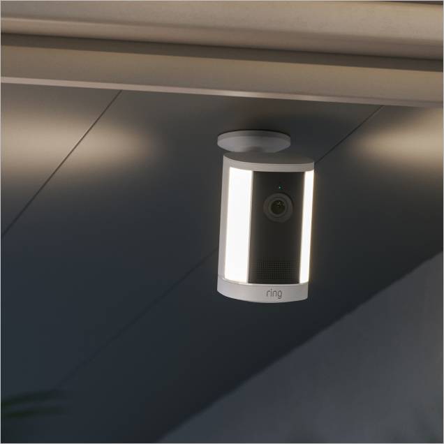 Ceiling-mounted Ring outdoor camera with dual vertical LED lights glowing at dusk on a covered porch.