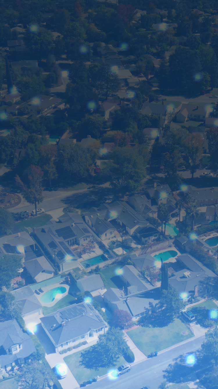 Aerial view of suburban neighborhood with houses, swimming pools, and trees, overlaid with blue tint and light spots.