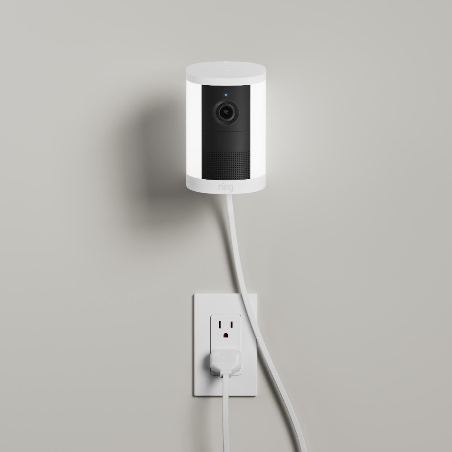Spotlight Cam (Newest Model) - Plug-In:White Ring Spotlight Cam (2nd Gen) mounted to a wall. Power cord stretches down the wall from the camera base.