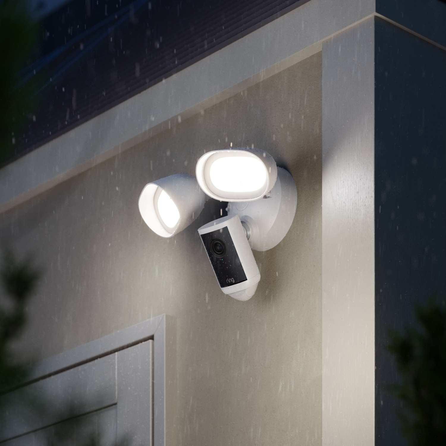 Floodlight Cam Pro (Newest Model) - White Ring Floodlight Cam Pro (2nd Gen) attached to a wall at dusk in the rain with floodlights illuminated 