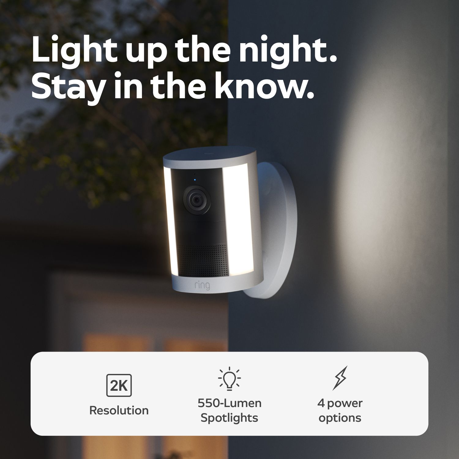 Spotlight Cam 2K - Wired:Wall-mounted Ring spotlight camera glowing at dusk, showing 2K resolution label, 550-lumen spotlights, and four power options.