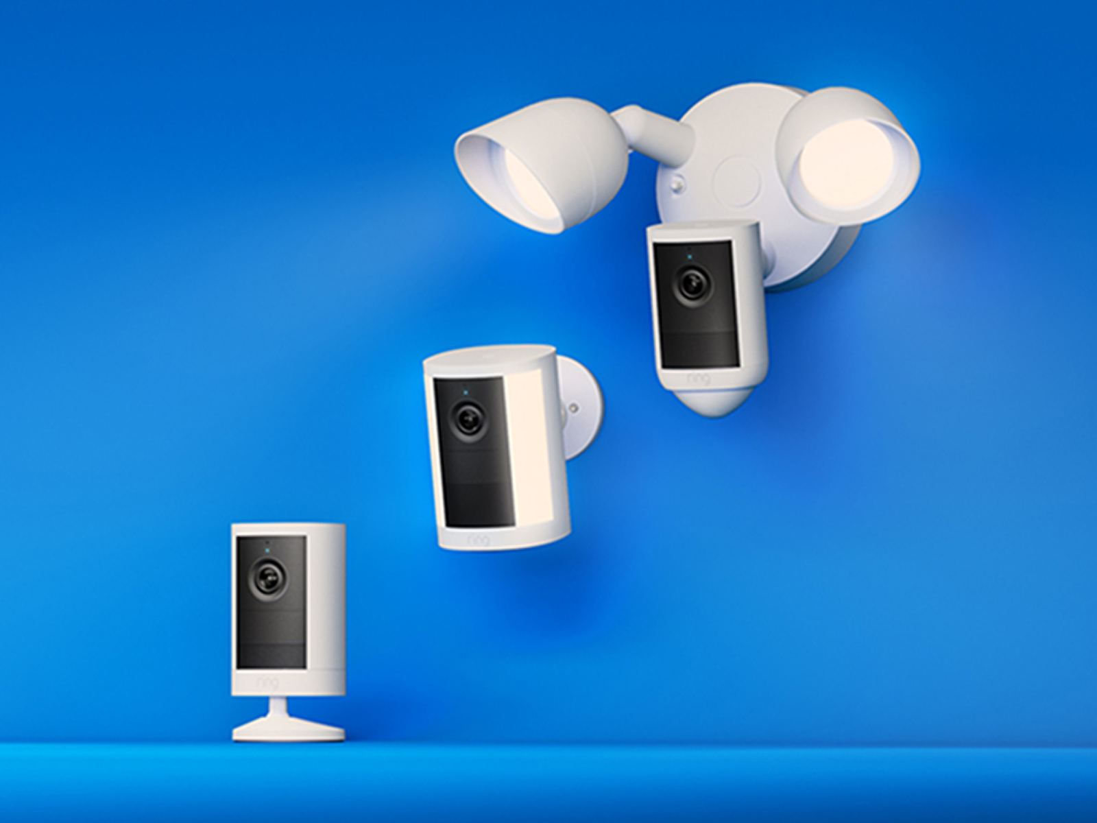 Two white Ring security cameras, one standalone and one with dual floodlights, mounted against a bright blue background.