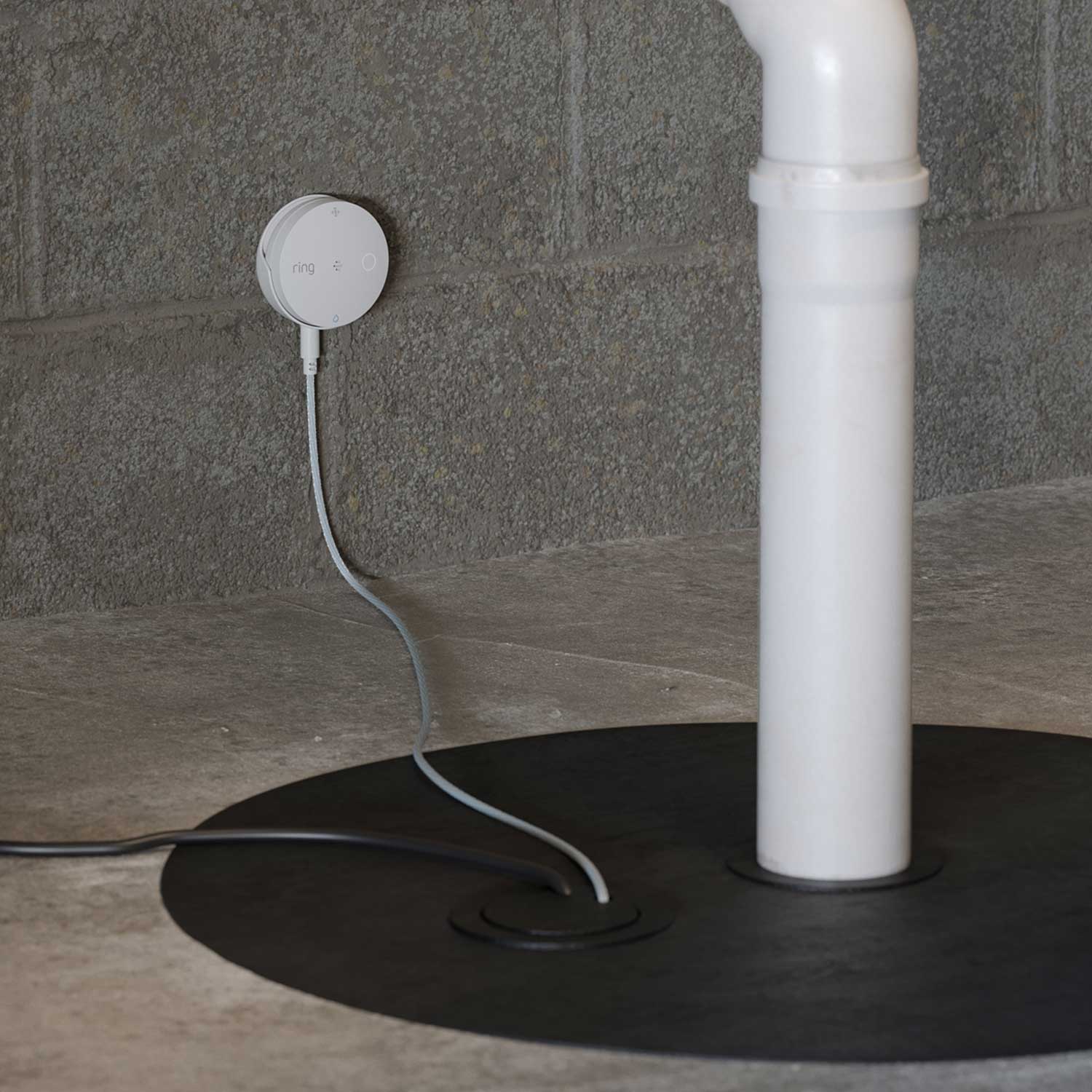 Sump Pump Monitor (Ring Sensors) - Ring alarm sensor mounted on concrete wall next to white PVC pipe, with wire running through floor opening.