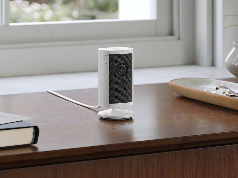 Ceiling-mounted Ring security camera with vertical LED lights, shown at dusk under an overhang.
